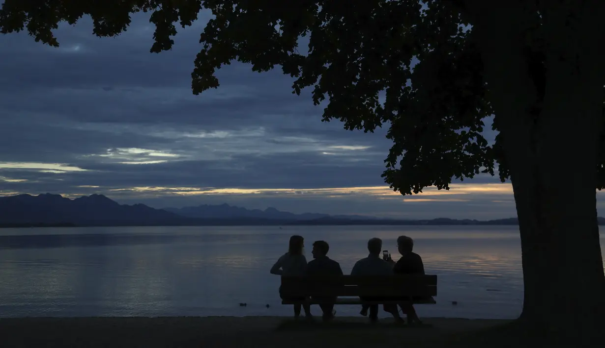 Orang-orang menikmati matahari terbenam di danau Chiemsee di Chieming, Jerman, Selasa, (25/8/2020). Chiemsee terbagi menjadi dua bagian, yaitu bagian timur laut yang lebih besar yang disebut Weitsee serta bagian Inselsee yang terletak di barat daya. (AP Photo / Matthias Schrader)