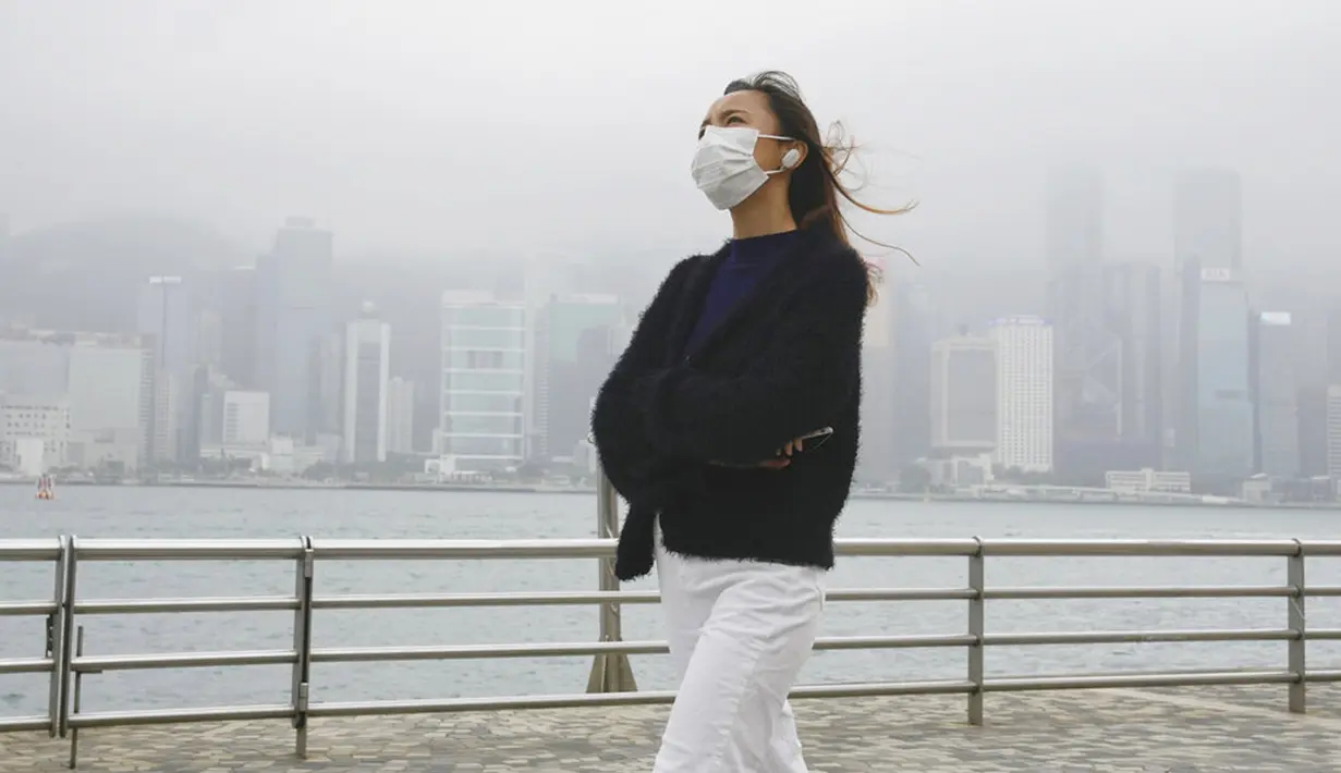 Seorang pria yang mengenakan masker berjalan di sepanjang jalan di Hong Kong, Jumat (28/1/2022). Hong Kong memangkas masa karantina wajib bagi orang-orang yang datang dari luar negeri dari 21 menjadi 14 hari. (AP Photo/Kin Cheung)