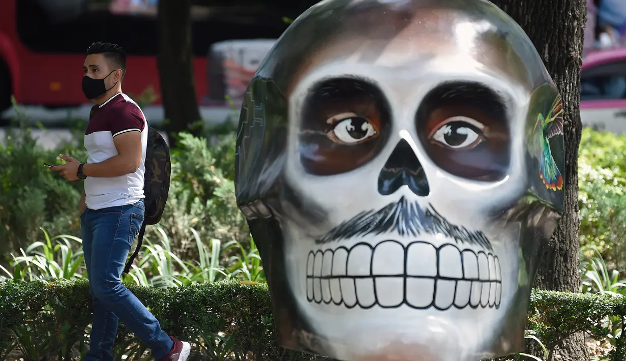 Seorang pria melewati tengkorak yang dihias selama pameran edisi keempat "Mexicraneos" (Mexisculls) di Reforma Avenue, Mexico City pada 23 Oktober 2020. Pameran tersebut karya seniman dari berbagai bagian negara Meksiko, dan juga dari Amerika Serikat serta Venezuela. (ALFREDO ESTRELLA/AFP)
