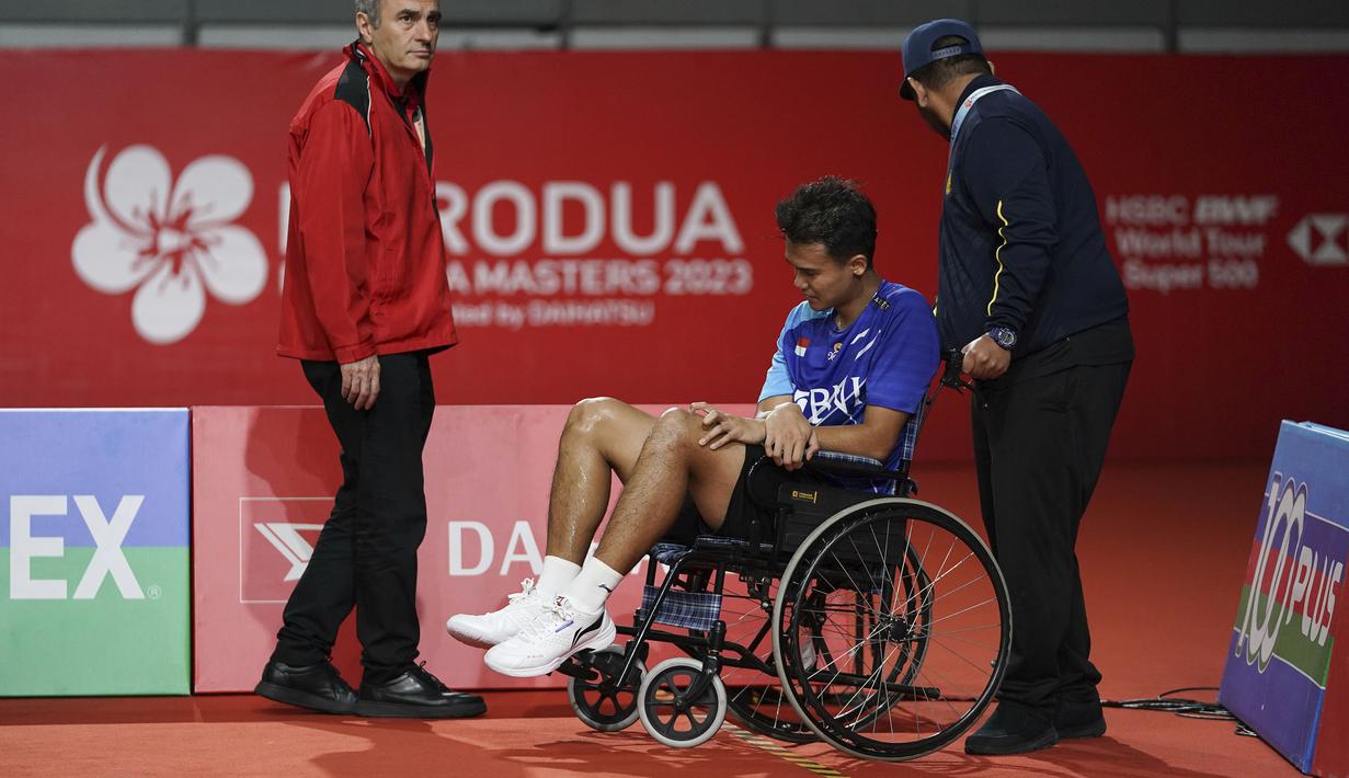 Pebulu tangkis Indonesia, Christian Adinata (tengah) meninggalkan lapangan dengan kursi roda saat semifinal tunggal putra Malaysia Masters 2023 melawan pebulu tangkis India, Prannoy HS di Bukit Jalil Axiata Arena, Kuala Lumpur, Malaysia, Sabtu (27/05/2023). Adinata gagal melanjutkan pertandingan karena cedera lutut saat ia tertinggal 17-19. (AP Photo/Kien Huo)