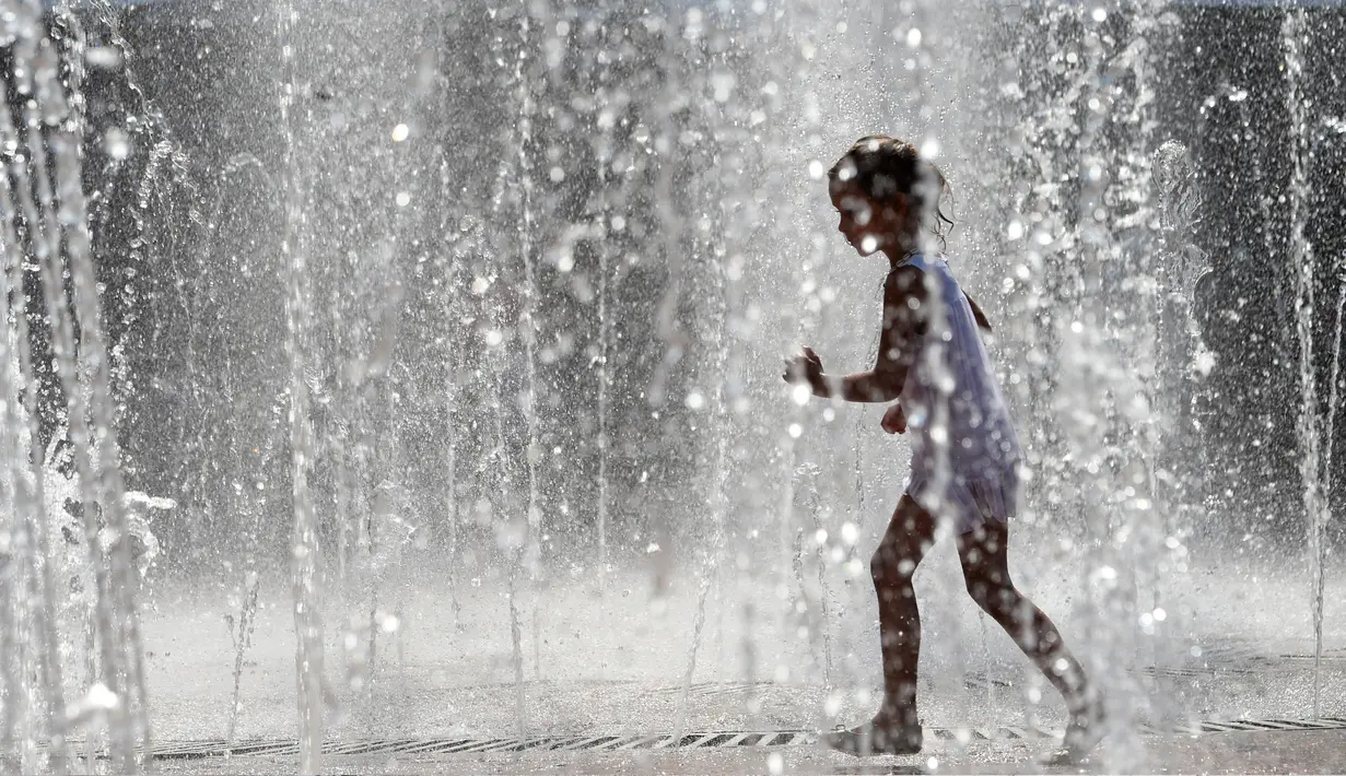 Seorang anak berjalan di air mancur selama gelombang panas di Kiev, Ukraina (20/8/2019). Panasnya cuaca yang ekstrem membuat anak-anak menyejukkan diri mereka di bawah guyuran air mancur. (AFP Photo/Sergei Supinsky)