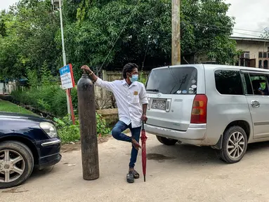 Seorang pria berdiri dengan tabung oksigen saat menunggu untuk mengisi ulangnya di luar sebuah pabrik di Yangon, Myanmar, Minggu (11/7/2021). Para pejabat mengatakan Myanmar mengalami lonjakan kasus COVID-19, memicu kelangkaan pasokan oksigen yang sangat dibutuhkan pasien. (Ye Aung THU/AFP)
