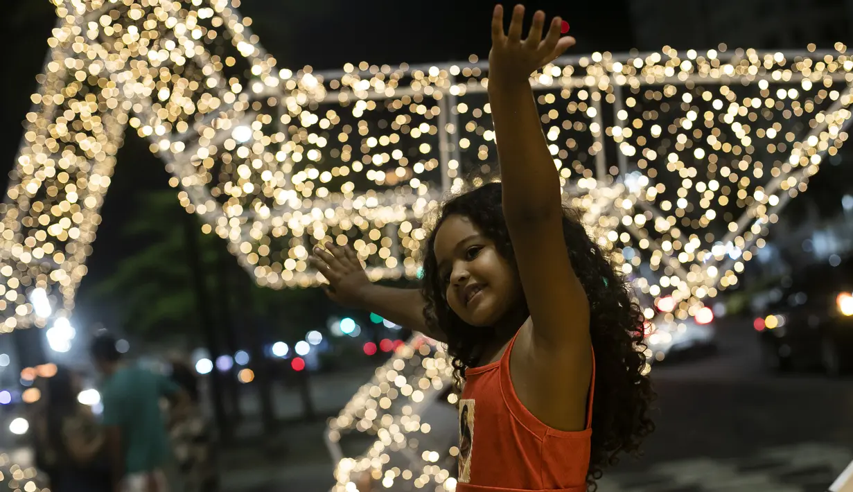Seorang anak berpose dengan latar belakang lampu Natal di sepanjang pantai Copacabana, di Rio de Janeiro, Brasil (11/12/2021). Jelang perayaan Natal, taman dan pantai dihiasi lampu-lampu yang indah. (AP Photo/Bruna Prado)