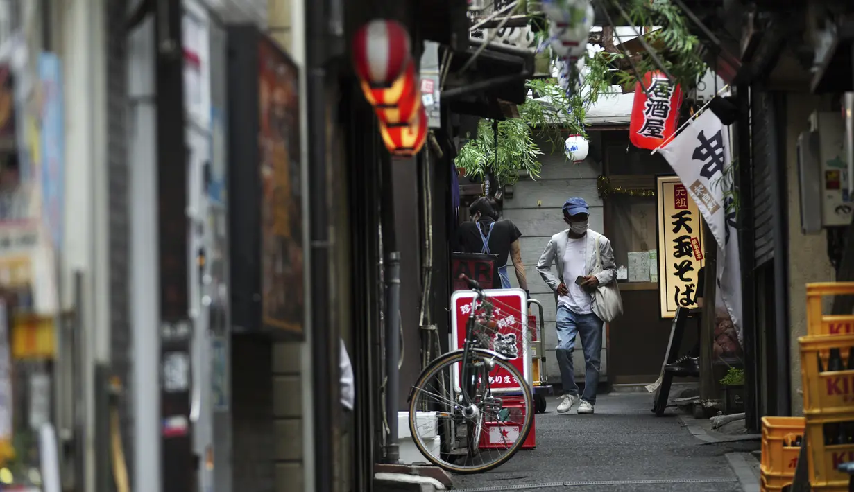 Seorang pria yang mengenakan masker untuk membantu mengekang penyebaran virus corona berjalan di sepanjang jalan bar yang kosong di Tokyo, Selasa (22/6/2021). Ibu kota Jepang mengkonfirmasi lebih dari 430 kasus virus corona baru pada hari Selasa. (AP Photo/Eugene Hoshiko)