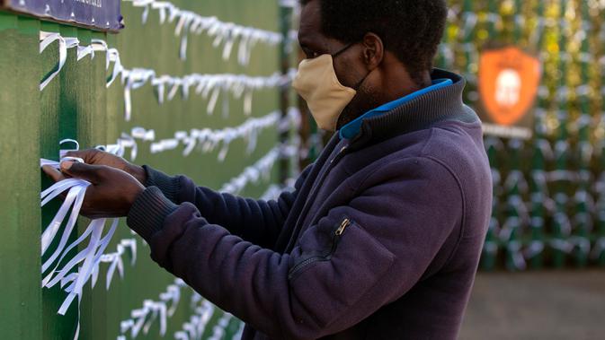 Leonard Makuya, seorang pengurus, mengikat pita ke pagar gereja St James Presbyterian di Bedford Gardens, Johannesburg, Rabu (29/7/2020). Pita tersebut mewakili warga Afrika Selatan yang meninggal akibat virus corona COVID-19. (AP Photo/Themba Hadebe)