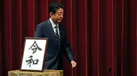 Perdana Menteri Jepang, Shinzo Abe berjalan melintasi plakat nama era baru Kekaisaran Jepang, Reiwa, seusai konferensi pers di Tokyo, Senin (1/4). Reiwa menjadi nama era yang baru yang mengganti Era Heisei seiring persiapan pengunduran diri Kaisar Akihito pada 31 April mendatang. (AP/Eugene Hoshiko)