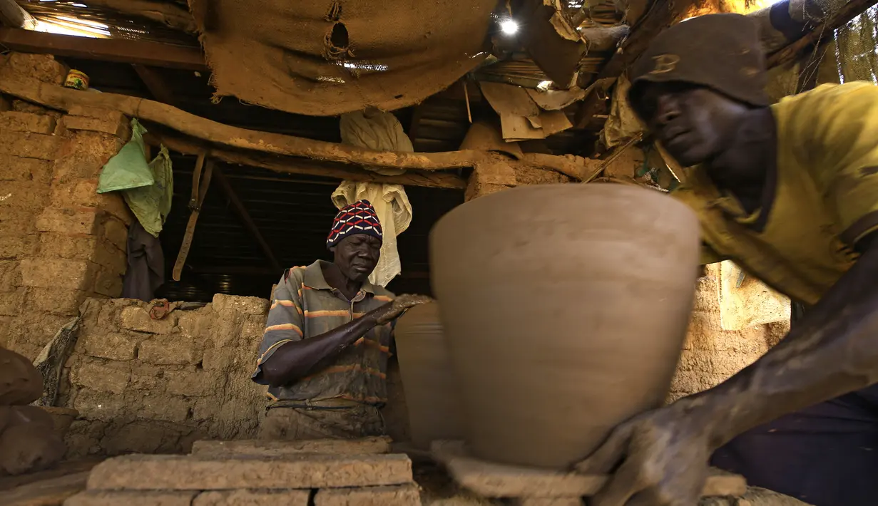 Seorang perajin Sudan membentuk sepotong tembikar di sebuah bengkel di Omdourman, di pinggiran barat ibu kota Khartoum (19/1/2022). Pot tanah liat tersebut nantinya akan dipajang untuk dijual. (AFP/Ashraf Shazly)