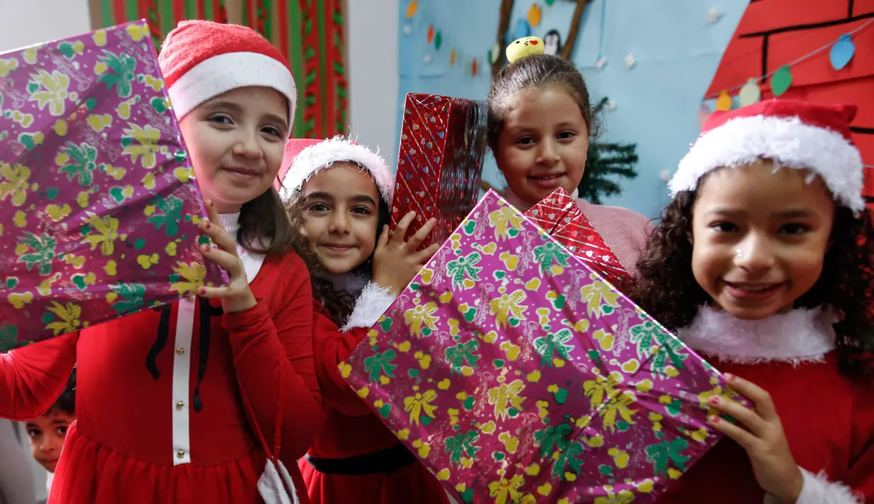 Sejumlah anak Palestina mengenakan kostum santa claus sambil membawa kado berpose saat perayaan menyambut Hari Natal di Sekolah Amerika di Kota Gaza (20/12).  (AFP Photo/Mohammed Abed)