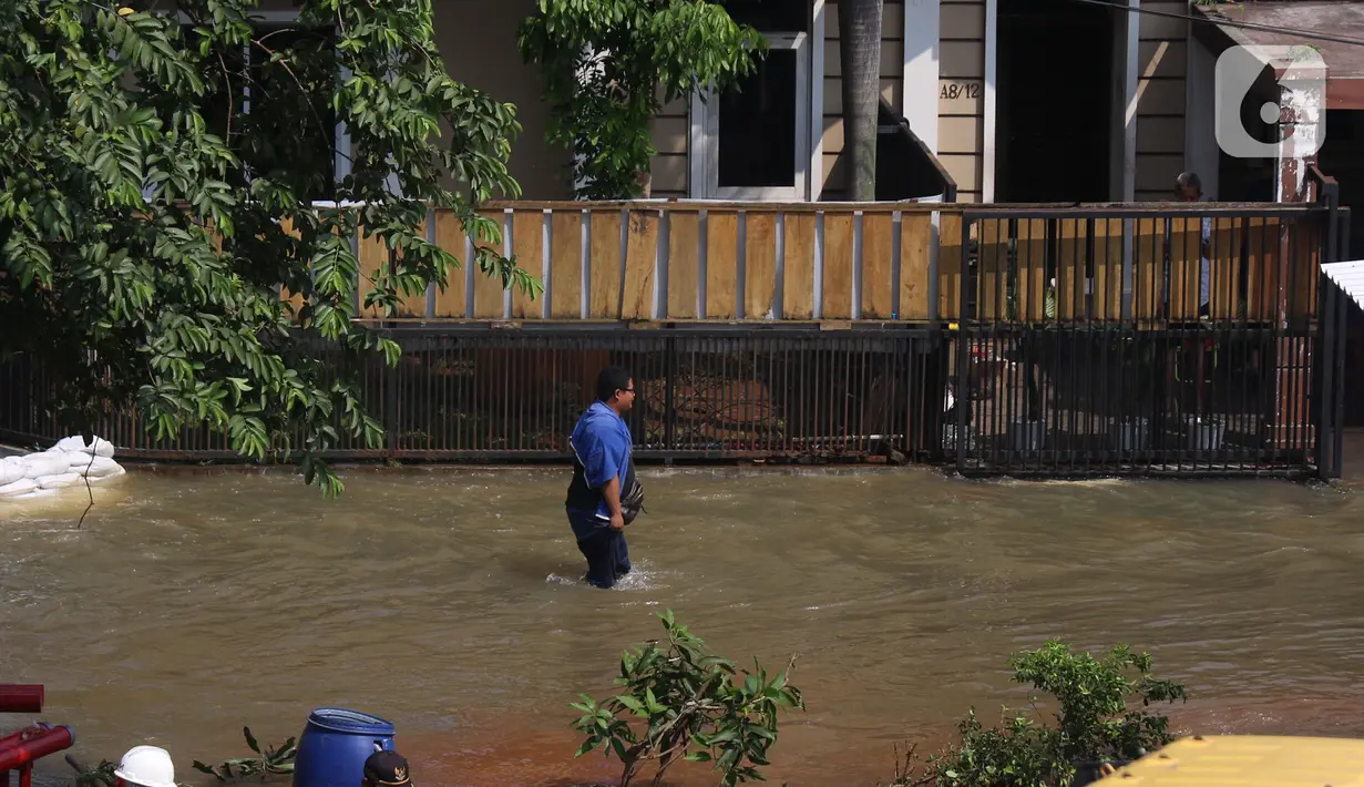 Warga melintasi banjir akibat jebolnya tanggul karena tertimpa tanah longsor, di Perumahan Nerada Estate Ciputat, Tangerang Selatan, Sabtu (12/6/2021). Longsor yang menimpa sejumlah rumah membuat tanggul pembatas kali jebol dan air meluap sehingga menyebabkan banjir. (Liputan6.com/Angga Yuniar)