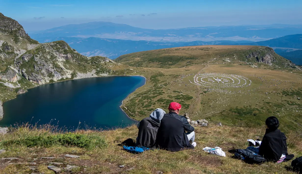 Sejumlah orang menyaksikan anggota gerakan keagamaan internasional White Brotherhood menari di puncak Gunung Rila, Bulgaria, Senin (19/8/2019). White Brotherhood didirikan oleh teolog Bulgaria Peter Deunov pada tahun 1897. (NIKOLAY DOYCHINOV/AFP)