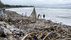 Orang-orang terlihat di samping tumpukan puing-puing dan sampah di di Pantai Kuta, Kabupaten Badung, Bali pada 26 Desember 2024. (SONNY TUMBELAKA/AFP)