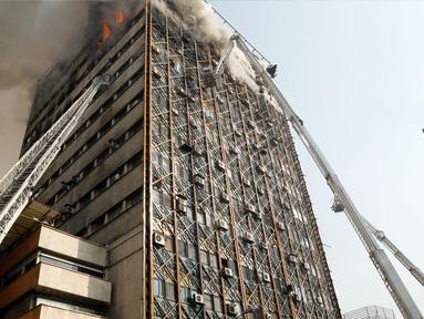 Petugas pemadam menggunakan crane mobil damkar untuk memadamkan kebakaran gedung tertua Iran, gedung Plasco, di pusat kota Teheran, Kamis (19/1). Sedikitnya 38 orang terluka akibat kebakaran di Gedung Plasco yang ikonik tersebut. (AFP PHOTO/STR)