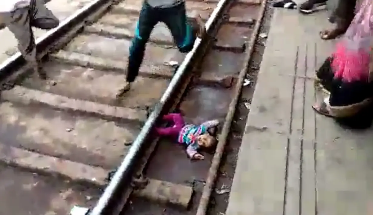 Gambar dari video pada 20 November 2018, bayi perempuan terjatuh dalam keadaan telentang di samping rel di stasiun kereta api di Mathura, Uttar Pradesh. Bayi satu tahun bernama Sahiba itu jatuh saat sebuah kereta melintas di atasnya. (NNIS / AFP)