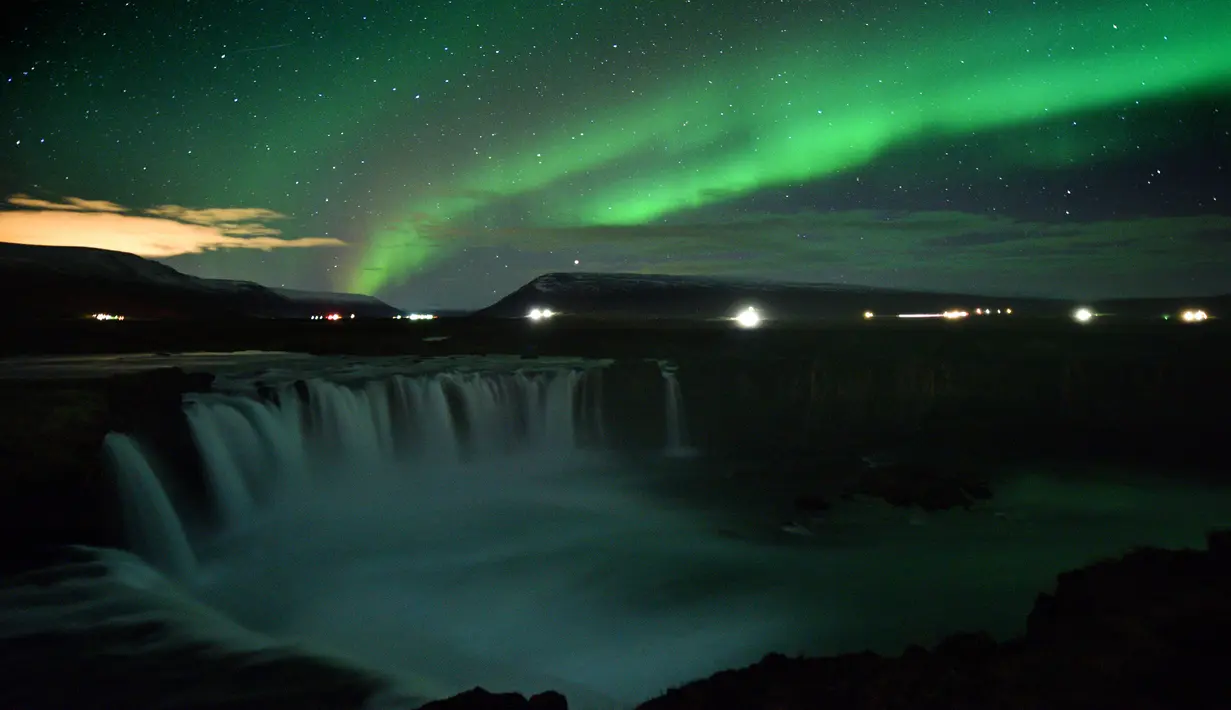 Langit berhias aurora borealis atau Cahaya Utara terlihat di atas air terjun Godafoss di Thingeyjarsveit, Islandia, 14 Oktober 2018. Lukisan abstrak alam semesta dari tabrakan spektrum warna Aurora Borealis begitu spektakuler. (Mariana SUAREZ/AFP)