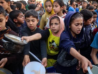 Anak-anak Palestina mendapatkan bagian dari makanan berbuka puasa untuk keluarga mereka di sebuah titik distribusi makanan gratis di kamp pengungsi Nuseirat, Jalur Gaza tengah, pada 14 Maret 2025. (Eyad BABA/AFP)