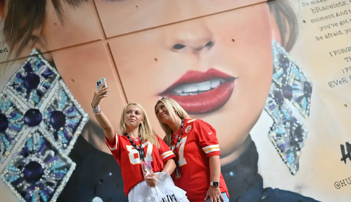 Penggemar Taylor Swift berswafoto dengan latar belakang mural sang penyanyi yang dibuat oleh seniman jalanan MurWalls, di luar Stadion Wembley, London, Kamis (15/8/2024). (JUSTIN TALLIS / AFP)