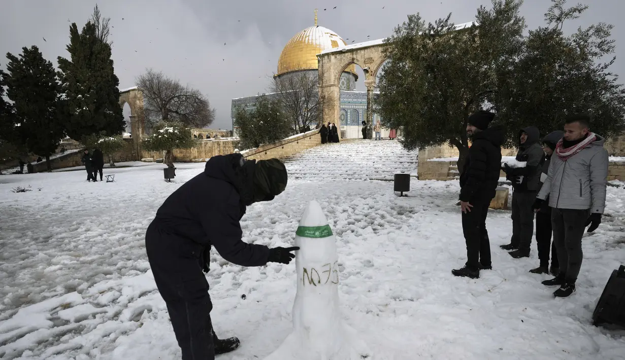 Seorang pria Palestina membuat patung salju berbentuk roket di sebelah Kubah Batu di kompleks Masjid Al Aqsa di Kota Tua Yerusalem, Kamis (27/1/2022). Hujan salju yang jarang melanda sebagian wilayah Israel dan Tepi Barat, menutup sekolah dan bisnis. (AP Photo/Mahmoud Illean)