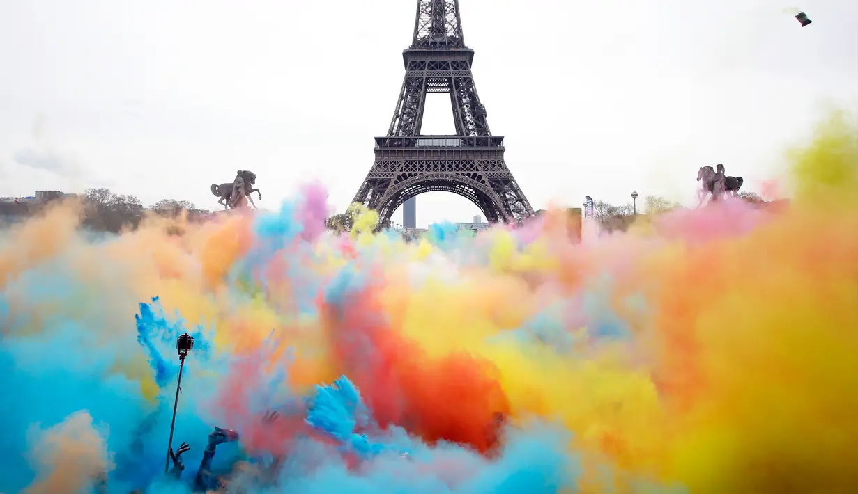 Sejumlah orang melempar bubuk berwarna saat merayakan akhir perlombaan Color Run 2018 di depan Menara Eiffel di Paris, Prancis (15/4). Dengan acara ini sekitar Menara Eiffel terlihat berwarna-warni. (AP/Thibault Camus)