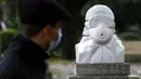 Seorang pria yang memakai masker wajah berjalan di dekat patung marmer yang didedikasikan untuk dokter, perawat, dan petugas kesehatan tanpa judul "Tentara anti Covid-19", di Taman Pincio di Roma tengah (4/11/2020). (AFP/Filippo Monteforte)