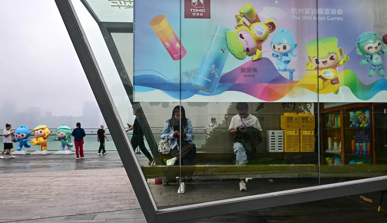 Orang-orang duduk di dalam stan yang dihiasi dengan poster Asian Games 2022 di sepanjang jalur pejalan kaki di sungai Qiantang di Hangzhou, provinsi Zhejiang, China pada 22 September 2023. (MANAN VATSYAYANA/AFP)