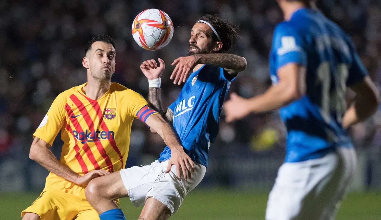 Gelandang Barcelona, Sergio Busquets (kiri) berebut bola dengan gelandang Linares Deportivo, Fran Carnicer pada babak 32 Besar Copa del Rey di Estadio Linarejos, Kamis (6/1/2022) dini hari WIB. Barcelona susah payah menang 2-1 atas tim divisi 3 Linares Deportivo. (JORGE GUERRERO / AFP)