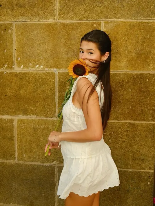 Maria Theodore tampil manis dibalut outfit serba putih memegang bunga matahari. Ia mengenakan atasan tanpa lengan dipadu celana pendeknya yang serasi. [Foto: Instagram/mariatheodoree]