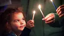 Riley Gillet (4) dari Orlando menyalakan lilin bersama keluarganya, menandai awal dari hari libur tradisional Yahudi Hanukkah, selama perayaan "Chanukah on the Park" Chabad of Greater Orlando di Winter Park, Florida, (28/11/2021). (Joe Burbank/Orlando Sentinel via AP)