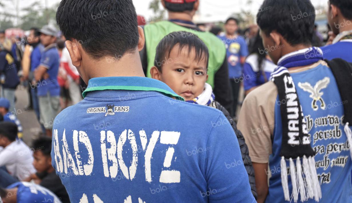 Seorang bobotoh menggedong anaknya saat hendak menonton Persib vs Bali United di Stadion Si Jalak Harupat, Bandung, Rabu (30/3/2016). Sang putra tampak anteng, tidak nakal alias Bad Boyz seperti tulisan di kaos sang ayah. (Bola.com/Nicklas Hanoatubun)