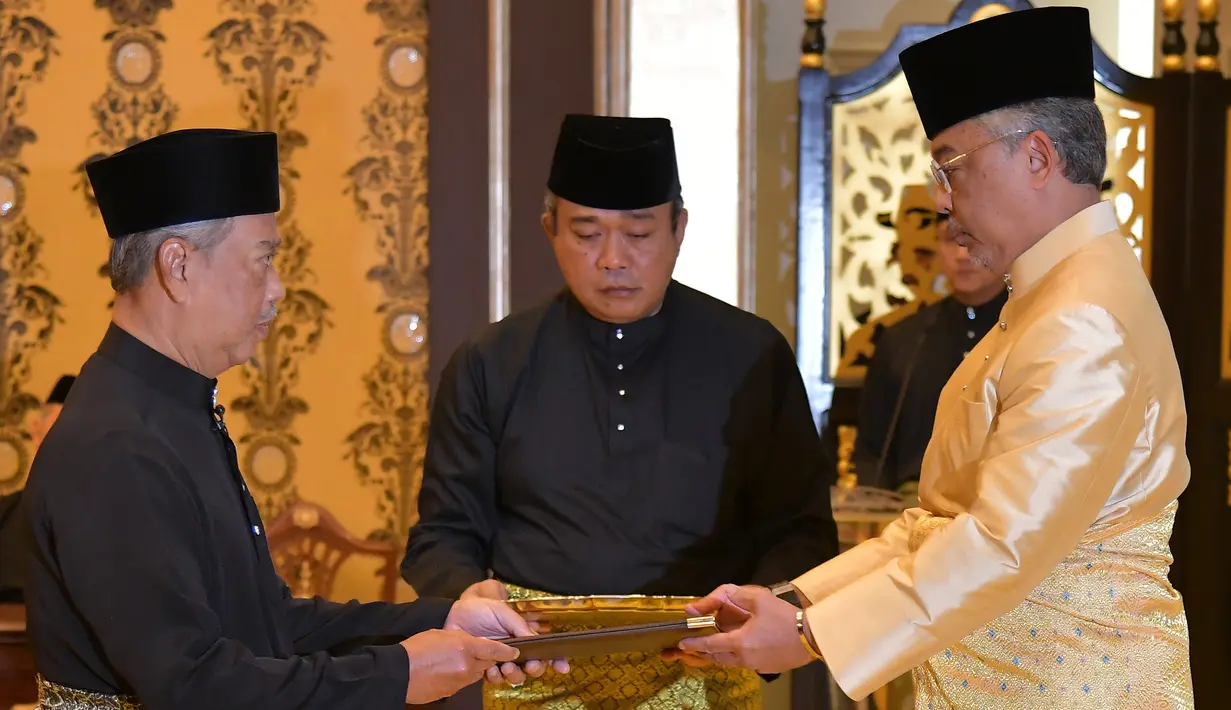 Muhyiddin Yassin (kiri) menerima dokumen dari Raja Sultan Abdullah Sultan Ahmad Shah (kanan) sebelum disumpah sebagai Perdana Menteri Malaysia di Istana Negara, Kuala Lumpur, Minggu (1/3/2020). Muhyiddin Yassin resmi menjadi PM Malaysia. (MASZUANDI ADNAN/MALAYSIA'S DEPARTMENT OF INFORMATION/AFP)