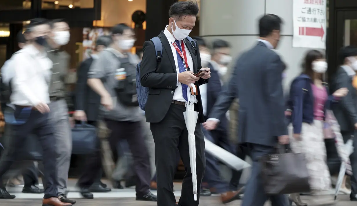 Seorang komuter melihat ponselnya saat orang-orang berjalan selama jam sibuk di Stasiun Shinagawa, Tokyo, Jumat (1/10/2021). Pemerintah Jepang mencabut keadaan darurat di semua wilayah pada 1 Oktober 2021. (AP Photo/Eugene Hoshiko)
