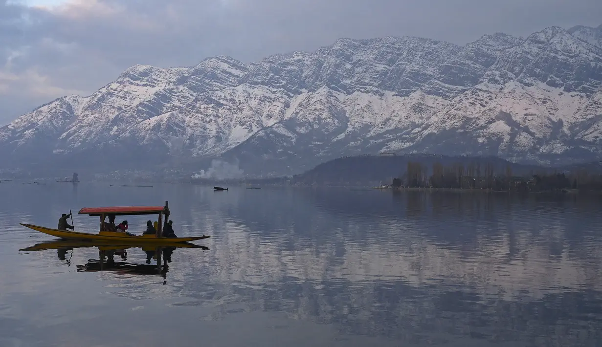 Orang-orang menikmati perjalanan dengan perahu dengan latar belakang pegunungan yang tertutup salju di danau Dal di Srinagar (11/1/2022). Danau Dal yang merupakan danau terbesar kedua di propinsi Jammu dan Kashmir negara bagian India ini merupakan pusat pariwisata dan rekreasi. (AFP/Tauseef Mustafa)