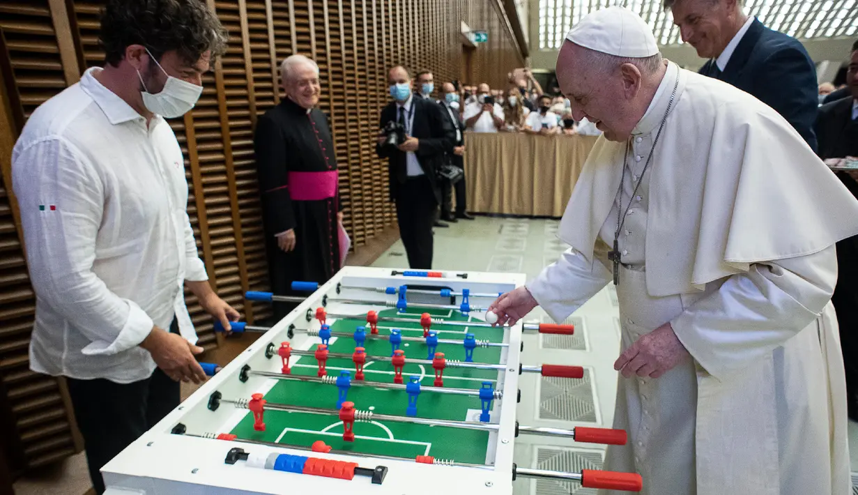 Paus Fransiskus bermain foosball atau sepak bola meja melawan Natale Tonini, presiden asosiasi Sport Toscana Calcio Balilla, pada akhir audiensi umum mingguan di Vatikan, Rabu (18/8/2021). Paus Fransiskus memang dikenal hobi bermain dan menonton sepak bola. (Vatican Media via AP)