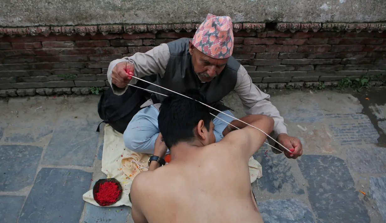 Seorang pemuka agama Hindu Nepal membantu pria mengenakan jimat Janai selama festival Janai Purnima di kuil Pashupati di Kathmandu, Nepal (28/7). Ritual ini bertujuan untuk memperoleh perlindungan dan pemurnian. (AP Photo / Niranjan Shrestha)