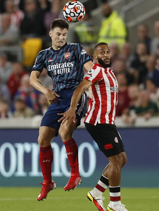 Bek Arsenal Kieran Tierney (kiri) menyundul bola di belakang gelandang Brentford Bryan Mbeumo (kanan) pada laga pembuka Liga Inggris 2021/2022 di Brentford Community Stadium, Sabtu (14/8/2021) dini hari WIB. The Gunners takluk 0-2 dari tim tuan rumah, Brentford. (Adrian DENNIS/AFP)