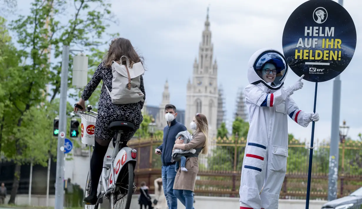 Seorang pesepeda diperlihatkan peringatan untuk mengenakan helm oleh siswa berkostum astronaut, di Ring Street, Wina, Austria, Rabu (5/5/2021). Delapan siswa Wina berpartisipasi dalam acara tersebut untuk mengingatkan pengendara sepeda mengenakan helm demi keamanan mereka. (JOE KLAMAR/AFP)