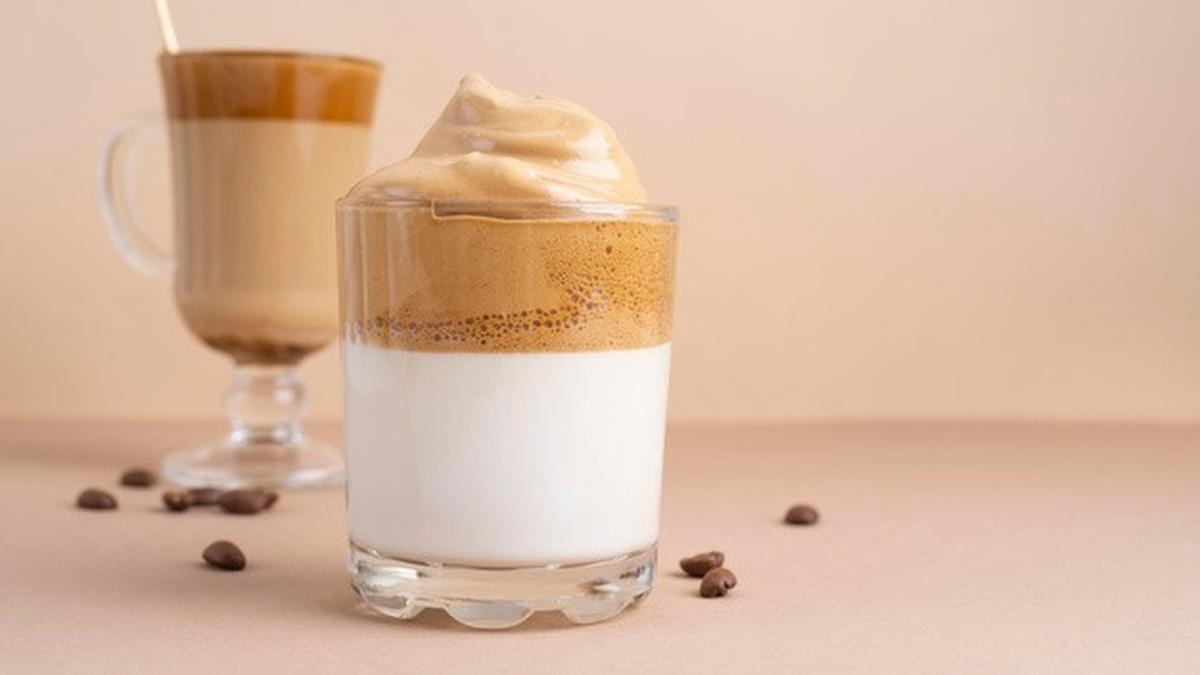 Cangkir kopi dalgona yang disajikan di atas meja kayu, menampilkan lapisan kopi tebal di atas susu putih, menciptakan kontras yang menarik dan sangat Instagrammable