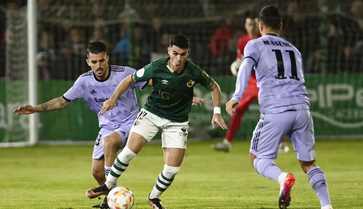Pemain Cacereno, Carmelo Merenciano membawa bola dari kawalan dua pemain Real Madrid, Dani Ceballos dan Marco Asensio selama pertandingan babak 32 besar Copa del Rey di stadion Principe Felipe di Caceres, Spanyol, Rabu (4/1/2023). Real Madrid menang tipis atas Cecereno dengan skor 1-0. (AP Photo/Pablo Garcia)