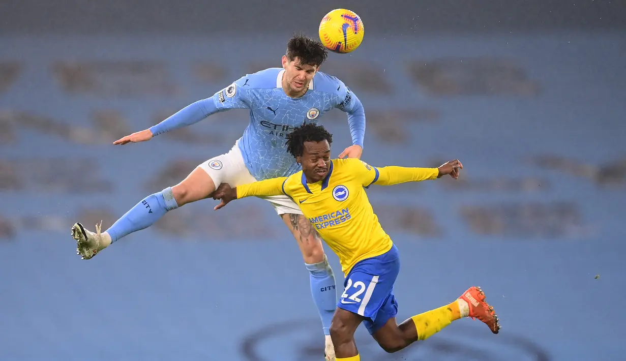 Bek Manchester City, John Stones (atas) memenangi duel udara dengan striker Brighton and Hove Albion, Percy Tau dalam laga lanjutan Liga Inggris 2020/21 di Etihad Stadium, Rabu (13/1/2021). Manchester City menang 1-0 atas Brighton. (AFP/Laurence Griffiths/Pool)