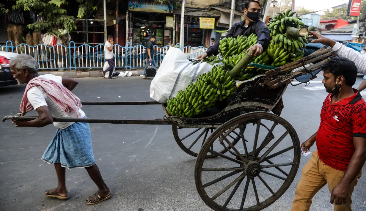 Seorang pria duduk di atas becak yang ditarik dengan tangan membawa pisang dan bahan-bahan lain untuk ibadah menjelang festival Hindu Chhat, di Kolkata, India (9/11/2021). (AP Photo/Bikas Das)