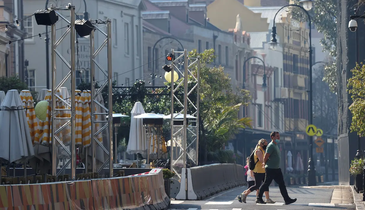 Orang-orang menyeberang jalan yang sepi di daerah Rocks Sydney (21/8/2021). Kota itu memperpanjang penguncian selama dua bulan dan memberlakukan jam malam sebagian untuk menahan wabah virus corona yang menyebar cepat. (AFP/David Gray)