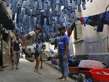 Anak-anak bermain bola di sebuah gang dengan jeans tergantung untuk dijual di pasar pakaian bekas di Kolkata, India, 10 Maret 2016. Kota ini memiliki kekurangan perumahan yang parah, setidaknya 1 juta orang tidur di jalan. (REUTERS/Rupak De Chowdhuri)