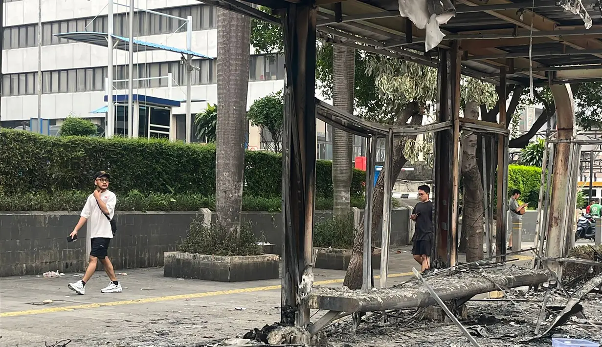 Warga melintas di sisi salah satu halte yang hangus di Jalan Jenderal Sudirman, Jakarta, Sabtu (30/8/2025). (merdeka.com/Arie Basuki)