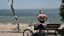 Seorang pria berdiri di sepanjang pantai menyaksikan orang-orang mandi di Thessaloniki, Yunani utara (23/6/2021).  Yunani bersiap menghadapi gelombang panas pertama musim panas, mendorong suhu siang hari ke wilayah 40+ Celcius di banyak bagian negara. (AFP/ Sakis Mitrolidis)