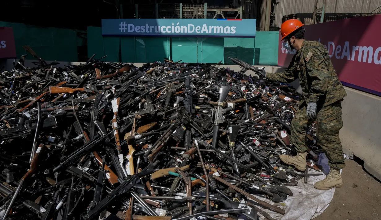 Seorang tentara berdiri di atas senjata yang secara sukarela diserahkan ke polisi atau disita sebelum dilebur di Santiago, Chile, Kamis (11/11/2021). Lebih dari 13.600 senjata ilegal dihancurkan, menurut komisi nasional yang mengatur senjata. (AP Photo/Esteban Felix)