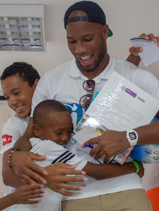 Mantan pesebak bola dunia Didier Drogba memeluk anak-anak saat melakukan acara amal organisasi internasional Peace and Sport, di Cartagena, Kolombia (19/3). (Cesar Carrion/Colombian Presidency/AFP)