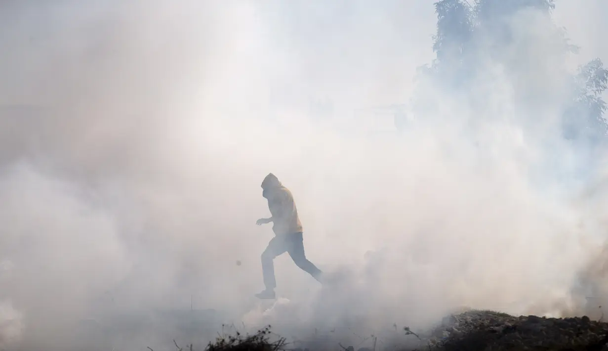 Seorang demonstran Palestina melarikan diri dari gas air mata yang ditembakkan oleh Israel selama protes terhadap permukiman Israel, di desa Tepi Barat Deir Jarir, utara Ramallah, Jumat (1/1/2021). (AP Photo/Majdi Mohammed)