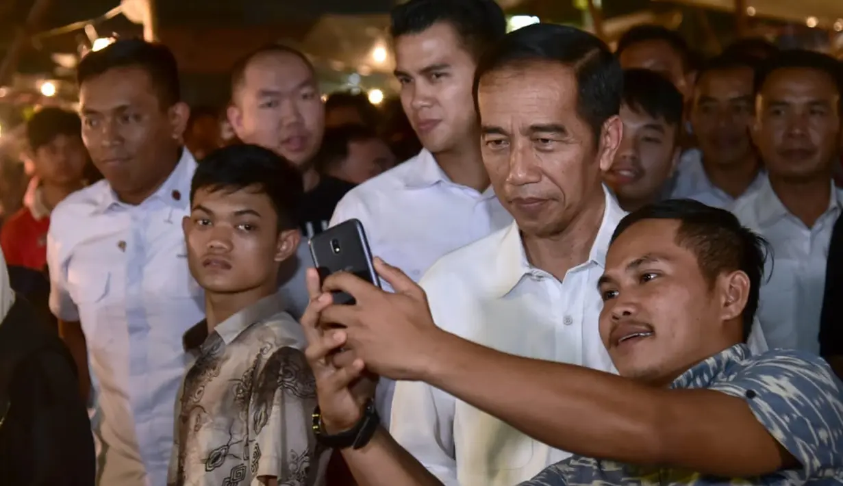 Seorang pria berswafoto dengan Presiden Joko Widodo (Jokowi) saat blusukan ke Pasar Bogor di Jalan Roda, Kota Bogor, Selasa (30/10) malam. Jokowi berinteraksi dengan para pedagang tentang harga bahan pokok. (Liputan6.com/HO/Biro Pers Setpres)