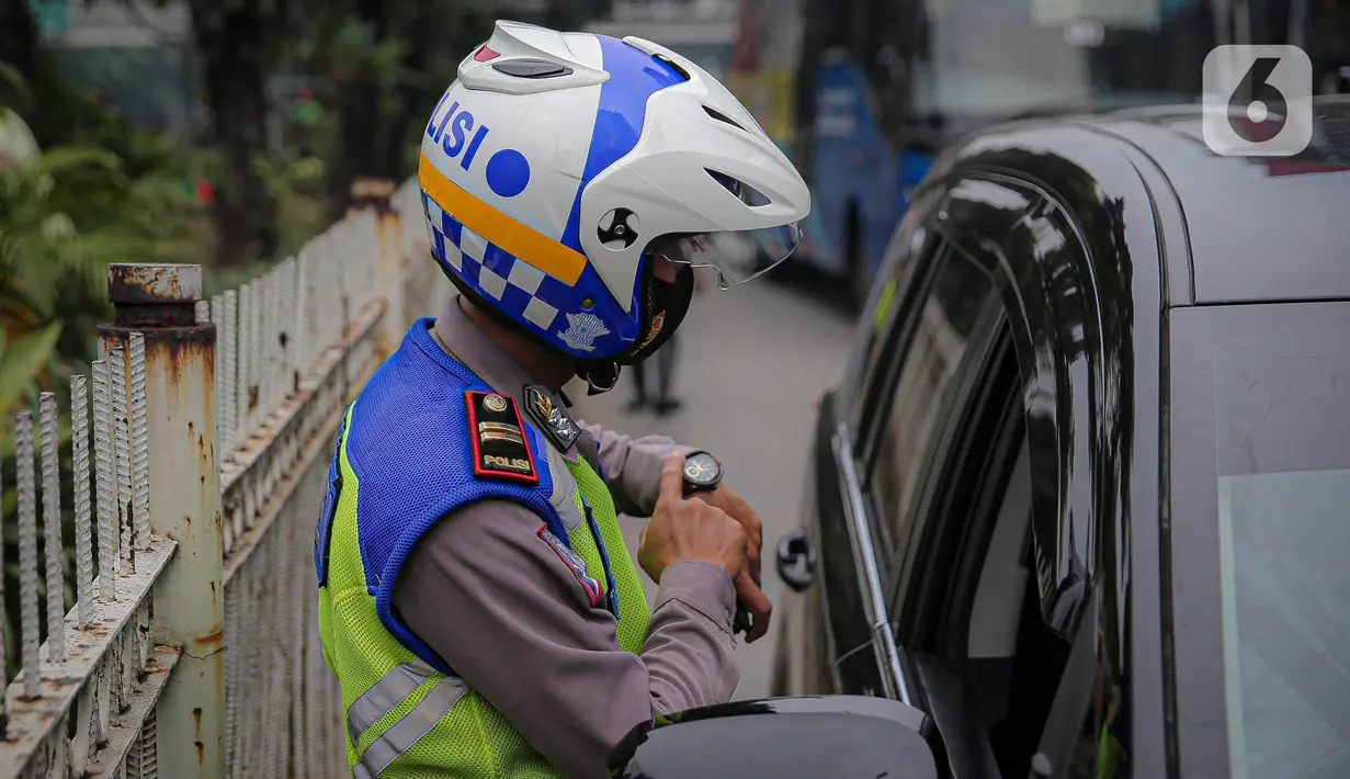 Anggota polisi melakukan penindakan kepada sebuah kendaraan saat ganjil genap di kawasan Jalan D.I Panjaitan, Jakarta, Senin (6/6/2022). Pembatasan mobil dengan sistem pelat nomor ganjil genap di Jakarta diperluas menjadi 25 titik mulai hari ini, Senin, 6 Juni 2022. (Liputan6.com/Faizal Fanani)