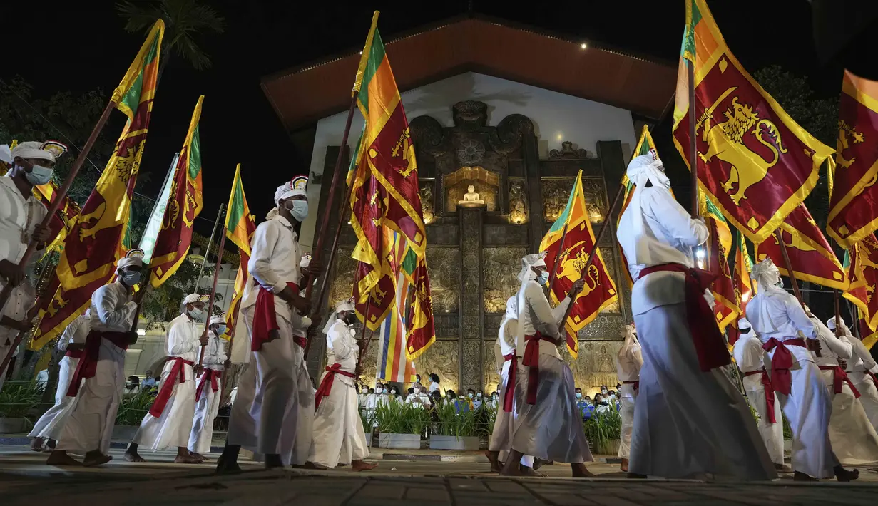 Warga mengenakan pakaian tradisional dan membawa bendera nasional pada Festival Navam Perahera di Kolombo, Sri Lanka, 15 Februari 2022. Biksu, penari, pemusik, dan lainnya berpartisipasi dalam perayaan di Kuil Gangaramaya yang terkenal. (AP Photo/Eranga Jayawardena)