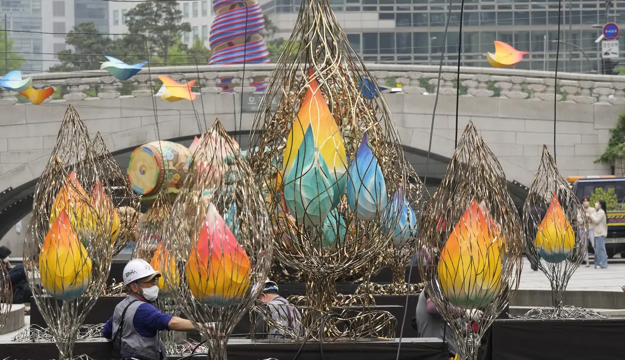 <p>Seorang pekerja mengenakan masker sebagai tindakan pencegahan terhadap penyebaran virus corona berdiri di tangga untuk mengatur kabel di dekat lentera untuk perayaan ulang tahun Buddha yang akan datang pada 8 Mei di Sungai Cheonggye di Seoul, Korea Selatan, Senin, 25 April 2022 (AP Photo/Ahn Young-joon)</p>